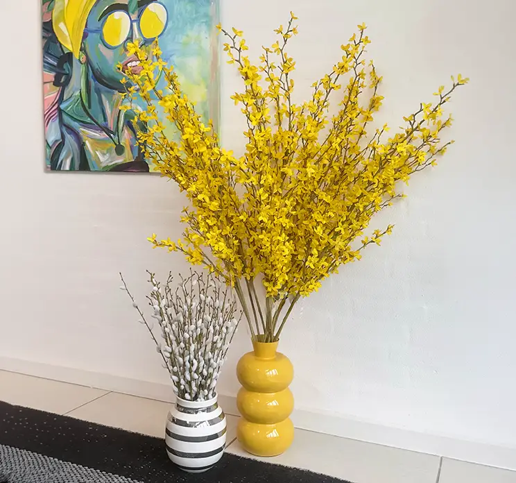 Forsythia og gæslingegrene kunstige grene sat i vaser på gulvet i køkkenmiljø