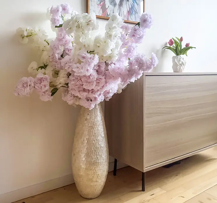 Kirserbærgrene med kunstige flydige blomster i hvid og lyserøde sat sammen i en vase i stuemiljø