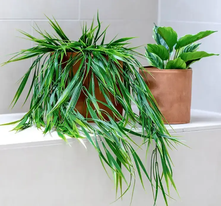 Kunstig græs hænger af plast i grøn vist i miljø hvor den er sat i en læderpotte