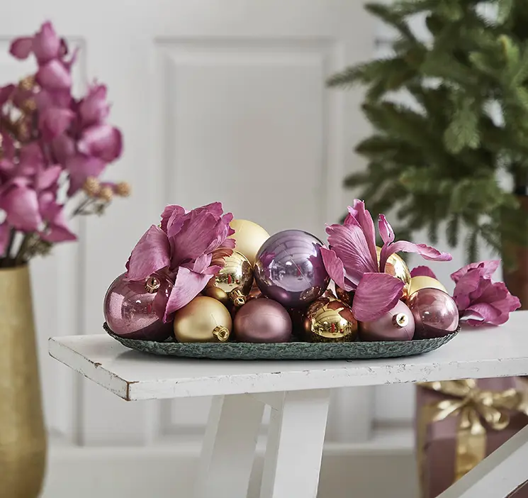 Iris kunstig blomst af plast i lyserød vist på fad med julekugler i guld, lyserød og lilla farver