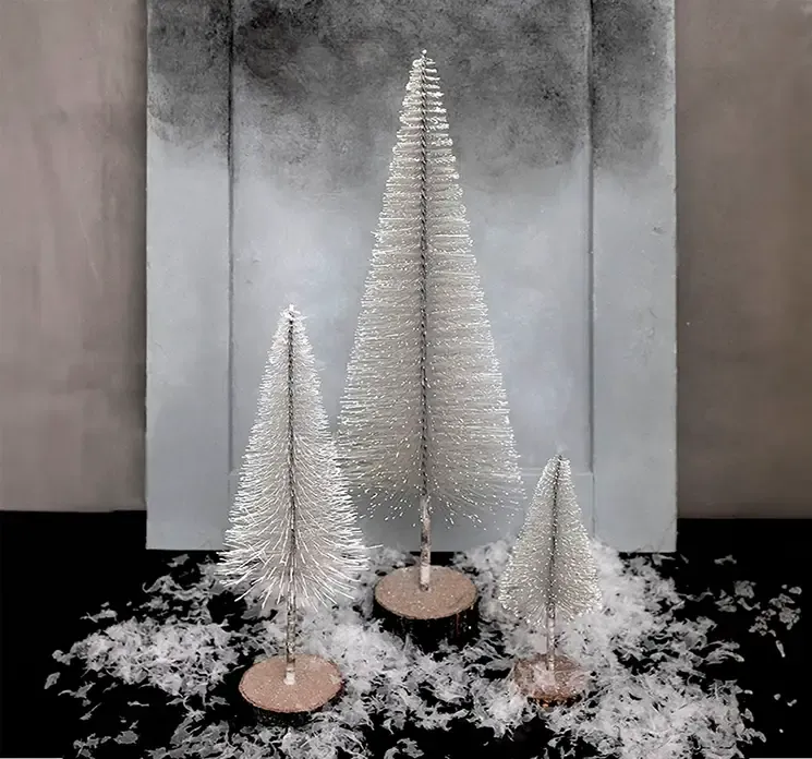 Kunstig børste juletræ af plast i brun på træfod vist i mijø med mindre træer og kunstig sne