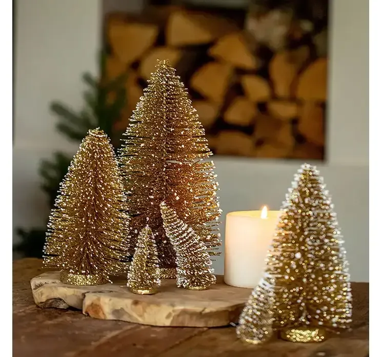 Kunstig børste juletræ plast i guld farvet på rund fod vist i miljø med børste træer i forskellige størrelser