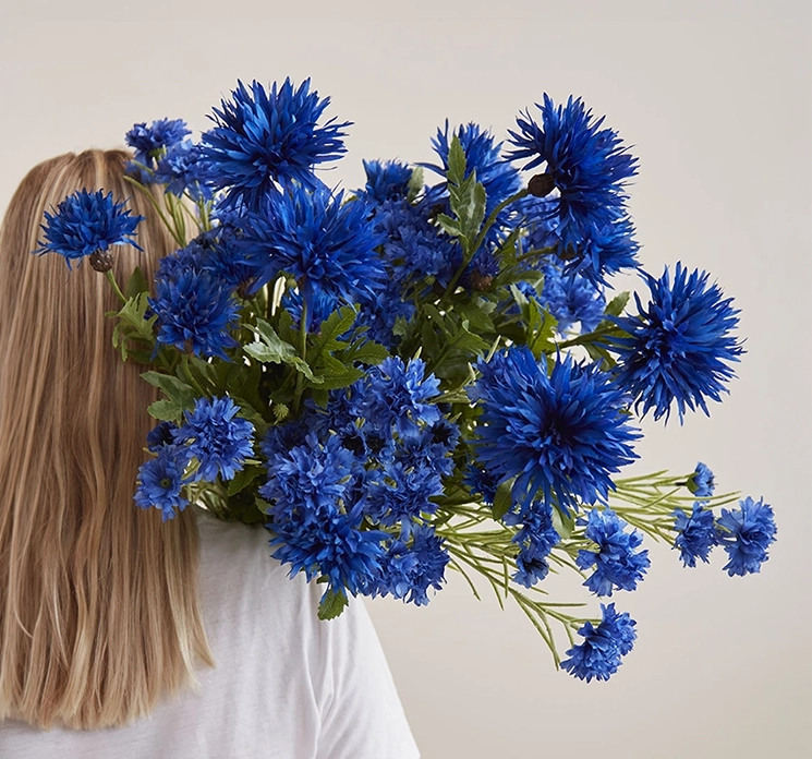 Kornblomster af plast i blå vist samlet i en buket holdt af dame, kunstig blomst