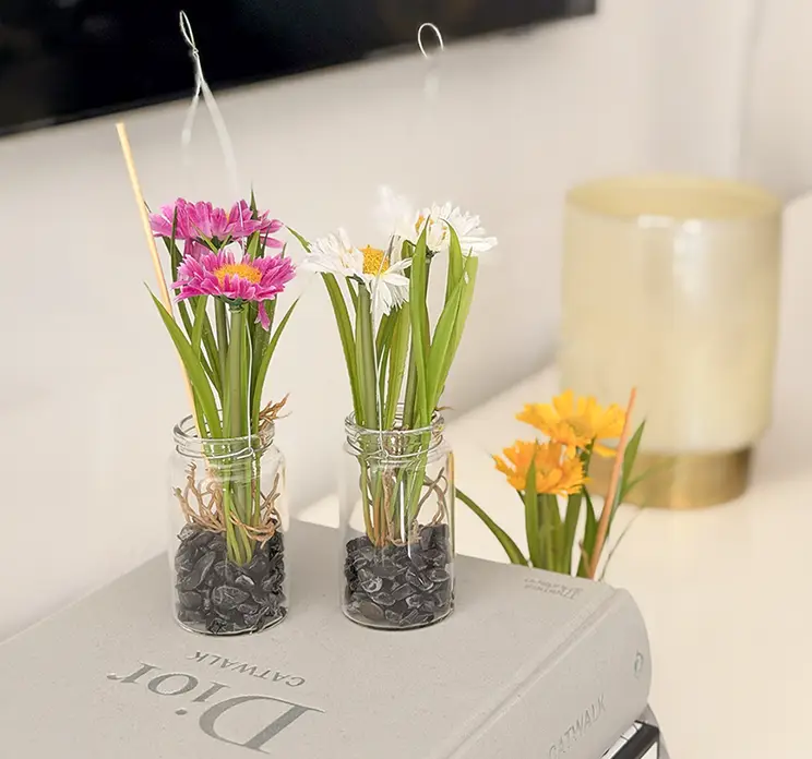 Margueritter kunstige blomster sat i glas vase med små sten og ophæng vist i stuemiljø