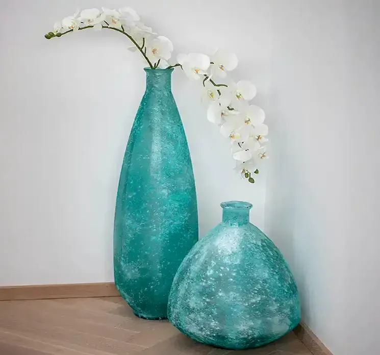 Kunstig orkide på stilk af plast creme farvet vist med to turkisfarvet vaser i miljø