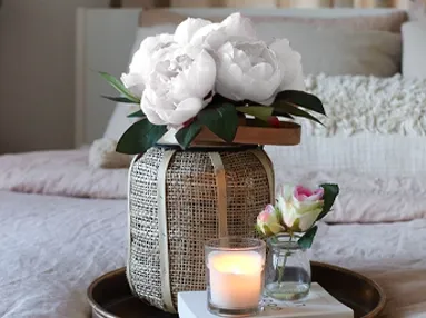 Fin lille kunstig pæon buket i hvid sat i en vase og en lille kunstig rose i glasvase på et fad