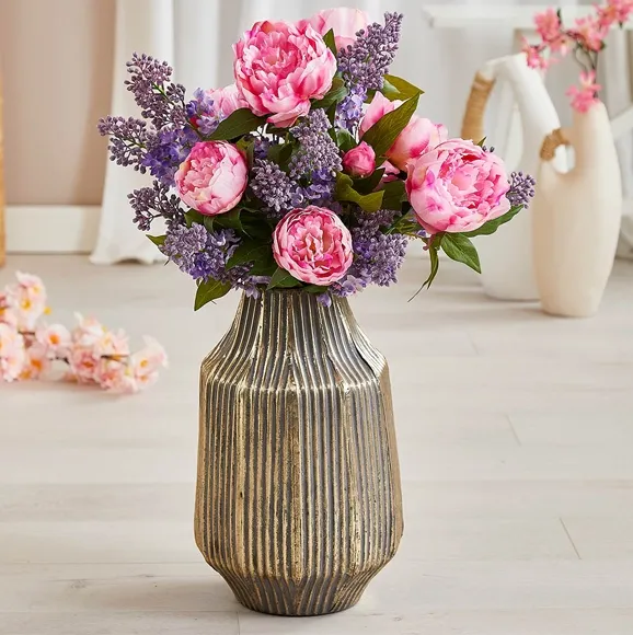 Kunstig buket af lyserøde pæoner og lilla syrener sat i en vase af metal