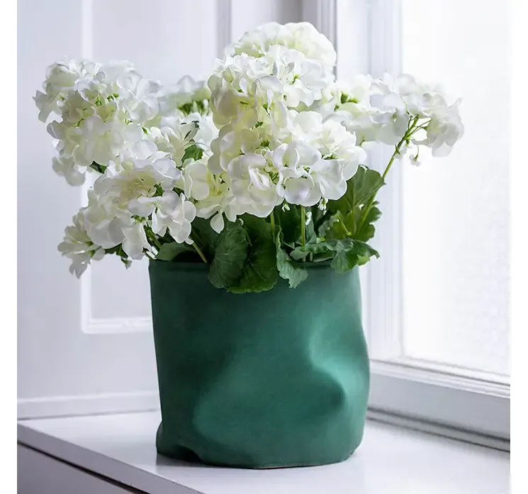 Potteskjuler i læder i grøn vist i miljø med hvid kunstig pelargonie blomst