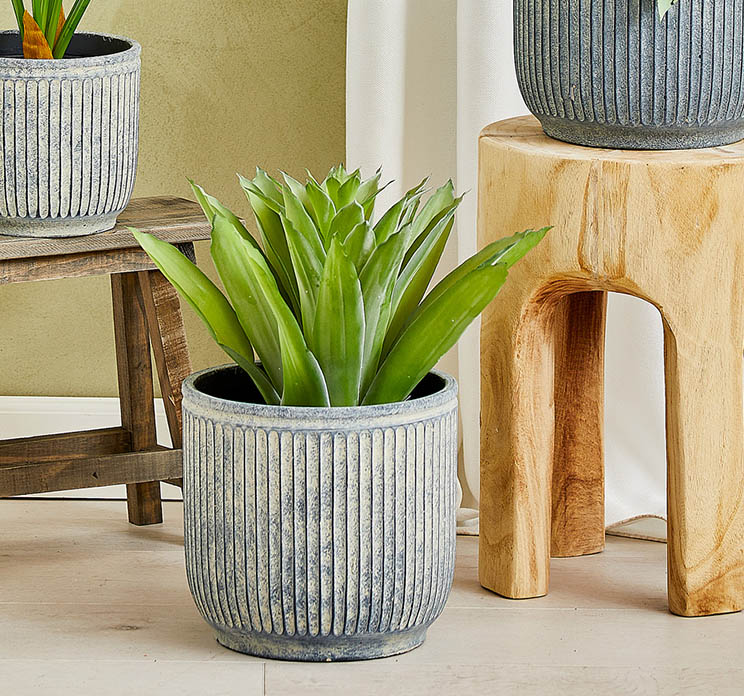 Kunstig agave plante i sort potte af plast vist i stuemiljø i cement krukke