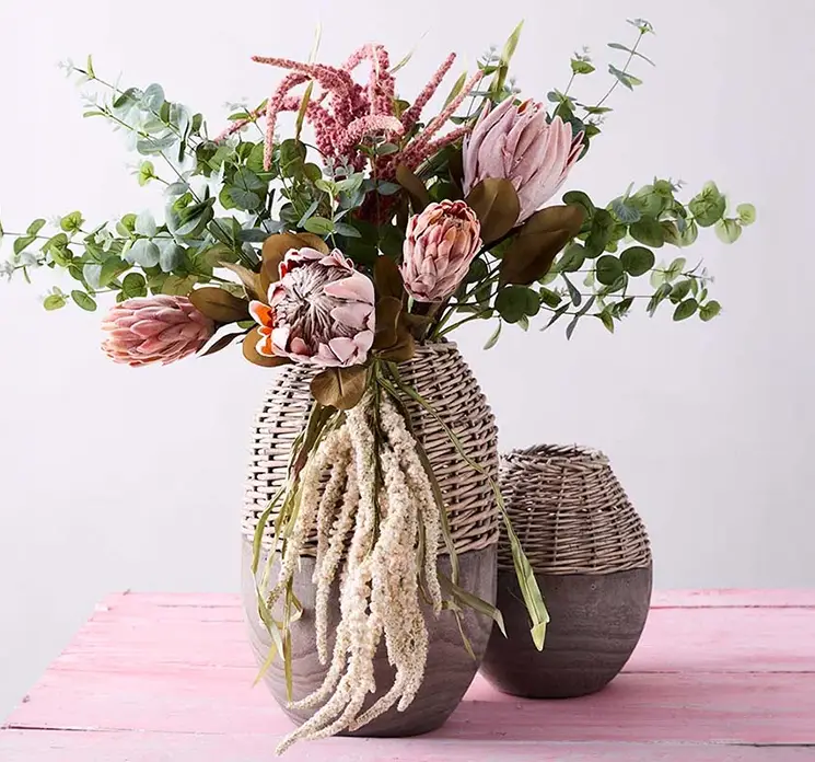 Protea tørret blomst af plast i fersken farvet vist med andre protea blomster i trævase med flet