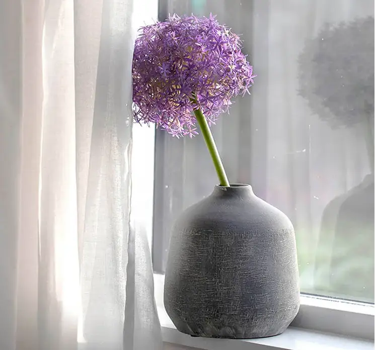 Prydløg kunstig blomst af plast i lilla vist i vase stående i vindueskarm