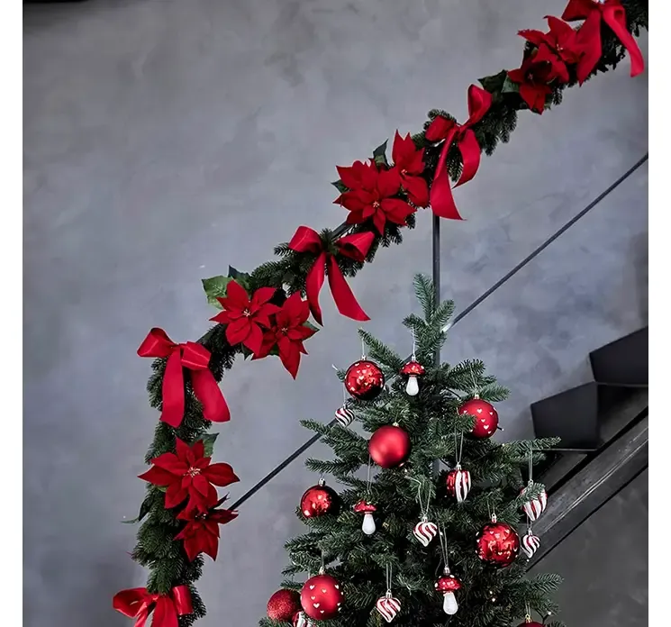 Kunstig granranke nisse af plast i grøn vist i miljø med røde sløjfer og kunstige julestjerner på et trappegelænder