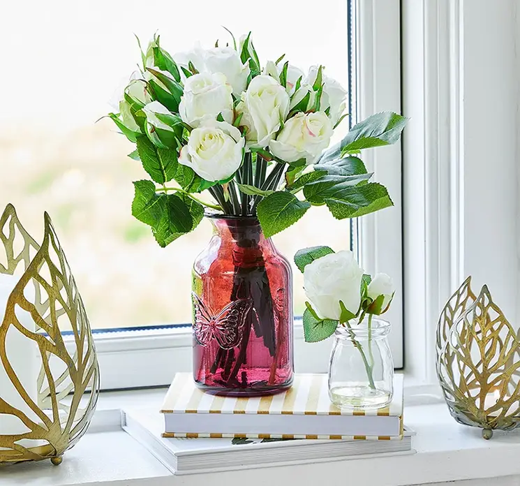 Rosenbuket kunstig blomst af plast med hvide roser sat i lille klar pinkfarvet glasvase i vindueskarm