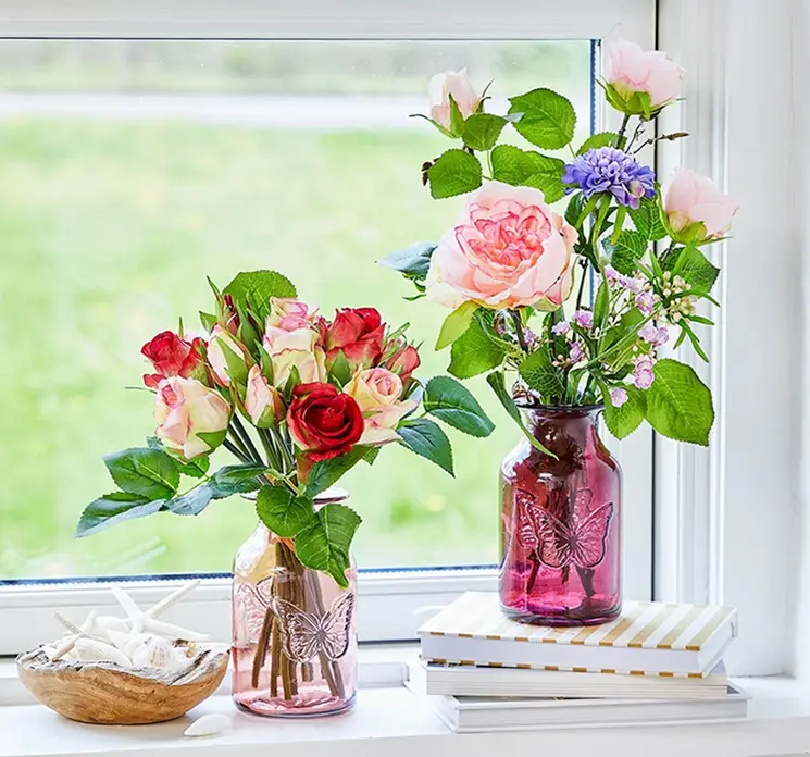 Rosen buket af kunstige blomster i røde og lyserøde farver vist vase med andre blomster i vindueskarm