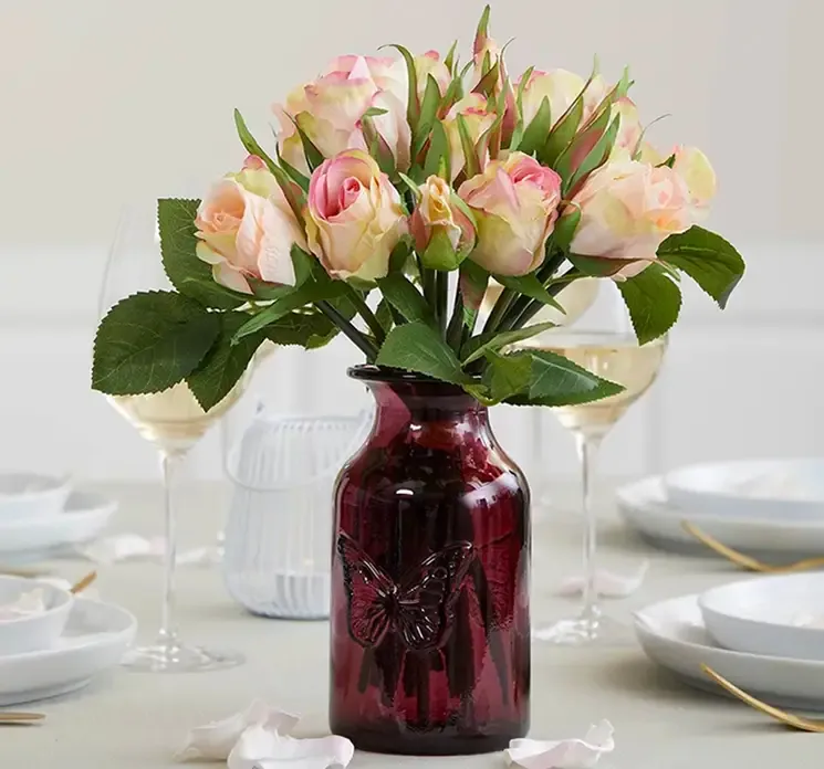 Glas vase i pink med sommerfugle imprint vist med kunstig rosenbuket på spisebord
