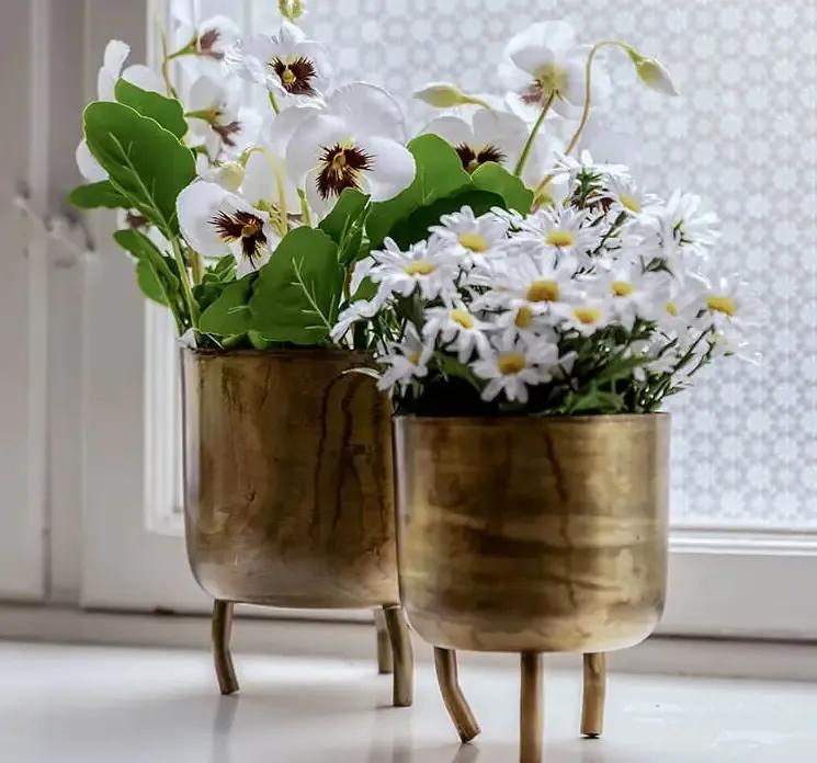 Blomster krukke med fødder af metal i guldfarvet vist i vindueskarm med kunstige blomster
