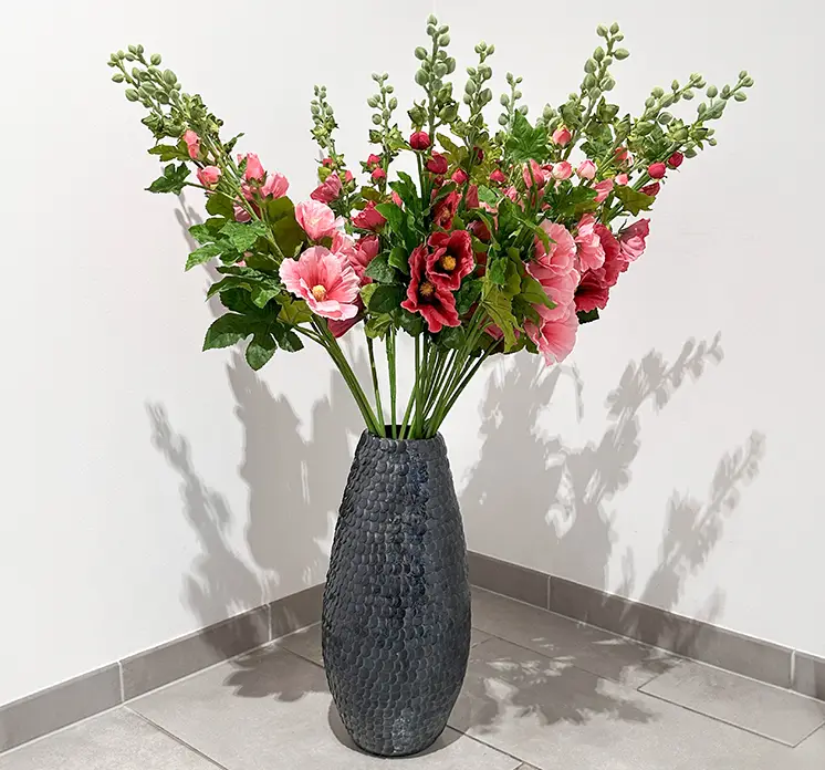 Vase med struktureret overflade i blå vist med kunstige stokroser på gulv i entre