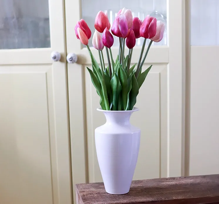 Vase i hvid jern vist i miljø med kunstige tulipaner i lyserøde nuancer