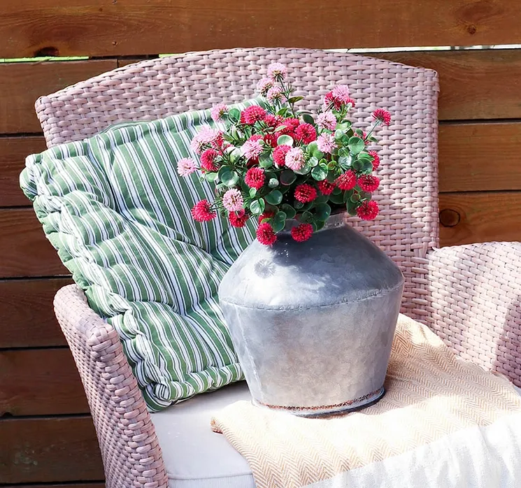 kunstig tusindfryd sat i en rund zinkvase på flettet havestol