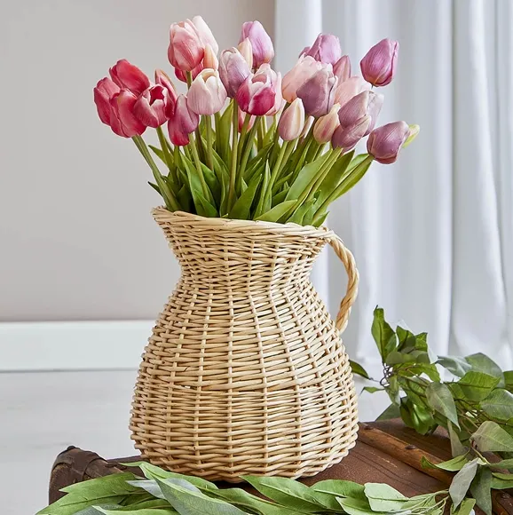 Flotte naturtro tulipaner i lyserøde og lilla farver sat i en fin fletvase formet som en kande