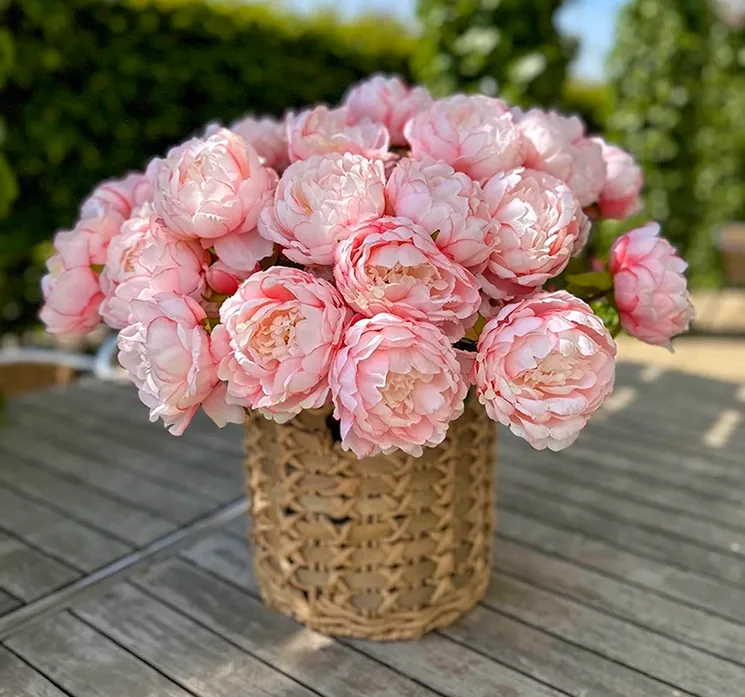 Kurvesæt af flettet rattan med plast vist i havemiljø med kunstige pæoner