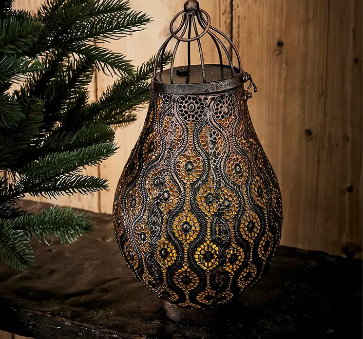 Lanterne med LED lys og fine udskæringer af metal i mørk kobber farve vist med lys i miljø