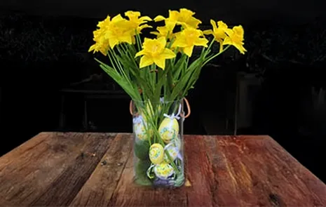 Kunstige påskeliljer med påskeæg og kunstige mossten i en klar glasvase