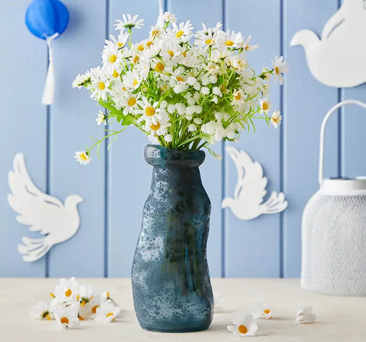 Marguerit buket af plast med hvide kunstige blomster vist i frostet blå vase og små papirsfugle som pynt i miljø
