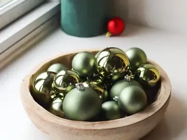 Træ skål fyldt med grønne plast julekugler i flere størrelser i en vindueskarm