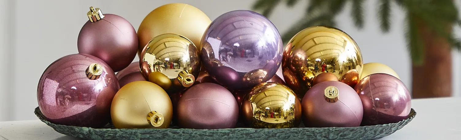 plastik julekugler på fad i rosa, lilla og guld farver