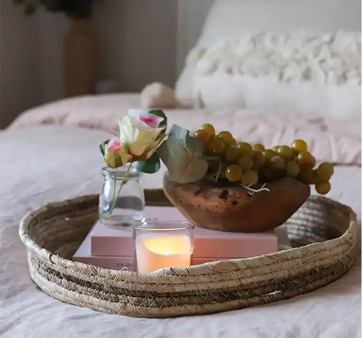 Rose kunstig blomst i creme farvet sat i lille glasvase vist på bakke med nips på seng