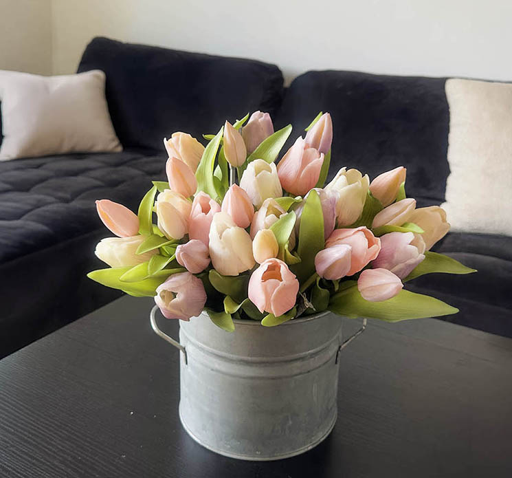 Tulipanbuket i pastelfarver sat i en rustik zink spand i stuemiljø