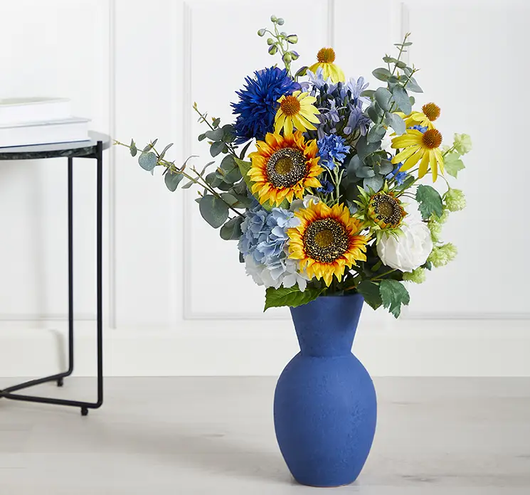 Vase i terracotta i blå vist med kunstige blomster som solsikker og kornblomster i stuemiljø