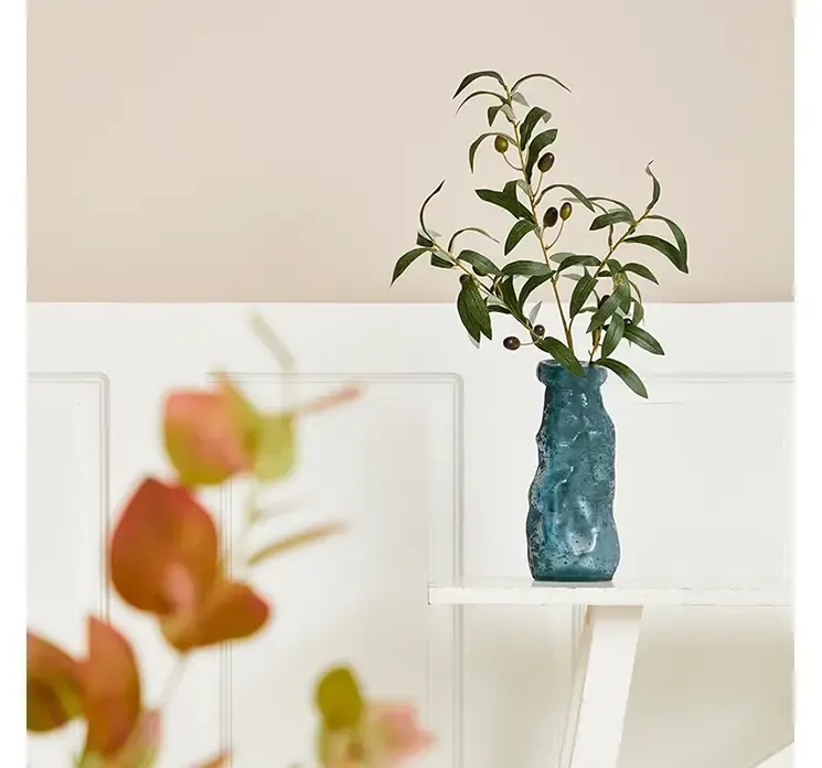 En enkelt kunstig oliven gren af plast i grøn med sorte oliven vist i en simplicity glas vase i miljø