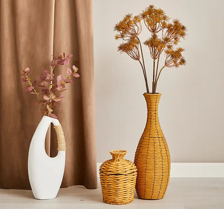 Vaser af flettet reb i naturfarvet og vase af papmache vist på gulv i stuemiljø med kunstige grene