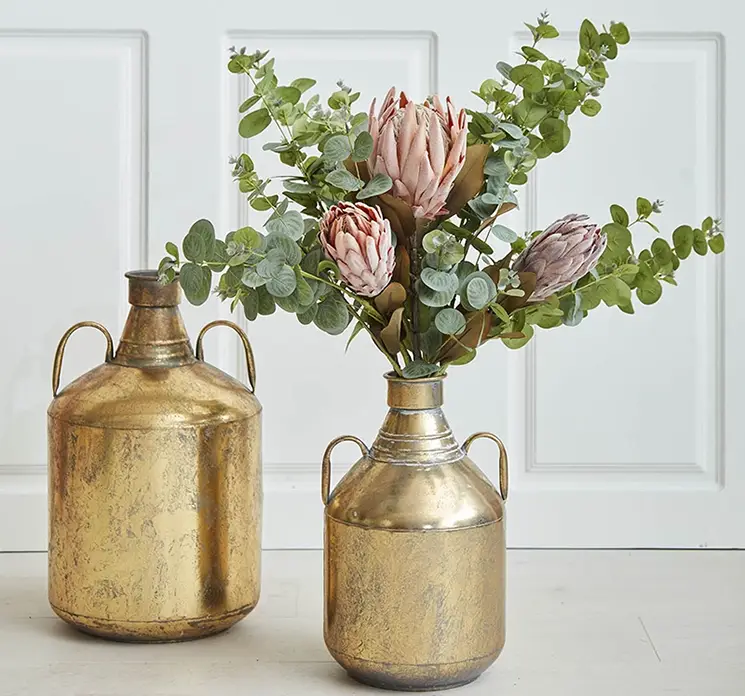 Protea kunstig blomst af plast i brun vist sammen med andre protea blomster i guldfarvet vase i stuemiljø